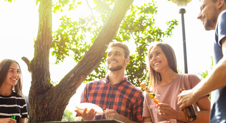 Happy friends grilling meat and enjoying barbecue party outdoors