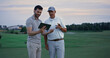 © stockbusters - Two golfers search tablet on field landscape. Happy men chatting online outside.