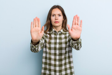 young adult pretty woman looking serious, unhappy, angry and displeased forbidding entry or saying stop with both open palms