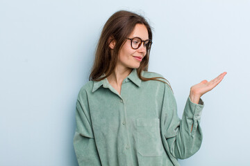 Wall Mural - young adult pretty woman feeling happy and smiling casually, looking to an object or concept held on the hand on the side