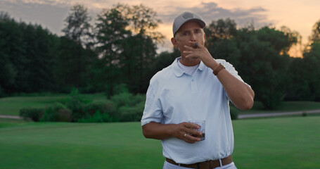 Wall Mural - Wealthy elderly smoke cigar on golf field. Old guy posing looking camera outside