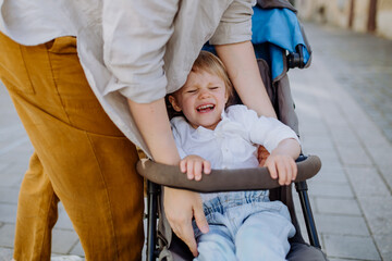 Mother calming a crying child sitting in a stroller while walking down the street