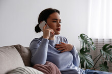 Portrait Of Upset Young Woman On The Phone With A Doctor Receiving Bad News. Sad Female Frowning, About To Cry. Copy Space For Text, White Wall Background, Close Up.
