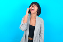 Overemotive Happy Young Businesswoman With Bob Haircut Wearing Blazer Against Blue Wall Laughs Out Positively Hears Funny Story From Friend During Telephone Conversation