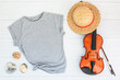 Close up gray blank template t shirt with copyspace and Summer Holiday concept. Top view mockup t-shirt with violin, staw hat and sea shells on white wood background. Summer music vacation background.