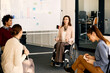 Female CEO in wheelchair talks to her colleagues while holding presentation in the office.
