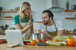 © gstockstudio - Young woman giving her husband to taste a meal while both standing at the kitchen