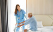 Smiling nurse helping elderly man get out of bed and walk around the room.