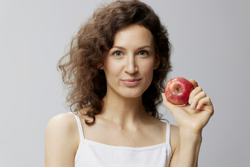 Wall Mural - Smiling lovely cute curly beautiful woman in basic white t-shirt pulls apple enjoy healthy food posing isolated on over white background. Natural Eco-friendly products concept. Copy space