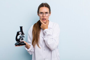 Wall Mural - young adult woman with mouth and eyes wide open and hand on chin. scientist with a microscope