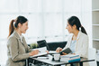 © PaeGAG - Young beautiful asian business woman is talking to her colleague, while sitting at the desk in a modern office. Concept of business success.