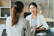 © PaeGAG - Young beautiful asian business woman is talking to her colleague, while sitting at the desk in a modern office. Concept of business success.