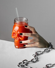 Halloween Concept - Close-up Of A Woman's Hand In Chains Reaching A Glass Of Bloody Juice In The Shape Of A Skull
