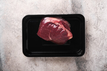 Wall Mural - Beef steak. Fresh raw beef steak with fork and rosemary in vacuum black plastic pack on grey stone background. Vacoom package. Top view. Mockup for design idea.