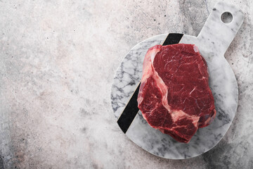 Wall Mural - Raw beef steak. Fresh beef rib eye steak with fork rosemary, salt and pepper on marble stand on grey stone background. Top view. Mockup for design idea.