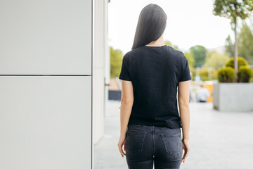 Wall Mural - Stylish brunette girl wearing black t-shirt and jeans posing against street , urban clothing style. Street photography