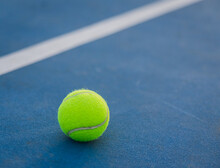 Close Up Of Yellow Tennis Ball On A Blue Hard Court.