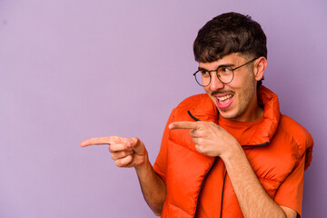 Wall Mural - Young caucasian man isolated on purple background points with thumb finger away, laughing and carefree.