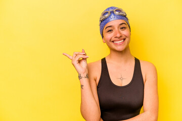 Wall Mural - Young swimmer hispanic woman isolated on yellow background smiling and pointing aside, showing something at blank space.