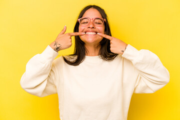Wall Mural - Young hispanic woman isolated on yellow background smiles, pointing fingers at mouth.