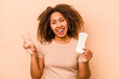 Young African American woman holding sanitary napkin isolated on beige background joyful and carefree showing a peace symbol with fingers.