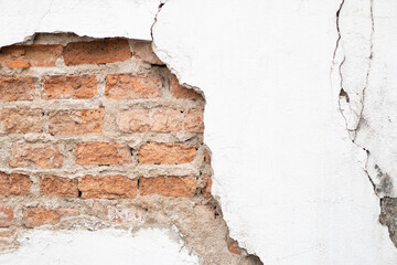 Cracked and broken white cement surface wall outside that shows the brick wall pattern inside of it