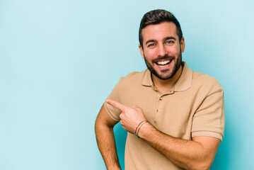 Wall Mural - Young caucasian man isolated on blue background smiling cheerfully pointing with forefinger away.