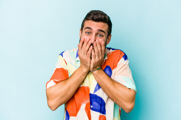 Wall Mural - Young caucasian man isolated on blue background laughing about something, covering mouth with hands.