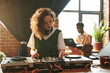 © pressmaster - Pretty girl with dark long wavy hair adjusting and mixing sounds by dj booth against young black man with laptop networking by window