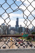 An Out Of Focus Shot Of The Downtown Chicago Skyline Framed By A Chain Link Fence With An Opening In It In Focus In The Foreground.