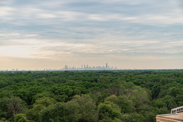 A beautiful aerial panoramic view of the downtown Chicago skyline in the distance with a yellow and blue cloud filled sky above and lush green treetops from a forest preserve below.