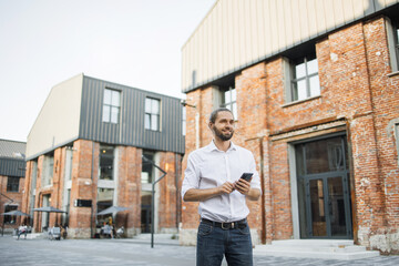 Wall Mural - Man using smartphone in a city. Smiling man looking at his mobile phone outdoors, modern lifestyle, connection, business, coffee break, communication, web chat, social media, apps concept.