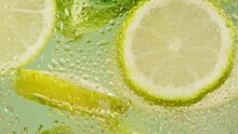 Lemon And Lime Cocktail, Cooking Cold Lemonade, Citrus Fruits In Water On Green Background, Shooting Of Carbonated Water With Floating Sliced Fruits. 
