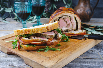 Canvas Print - Traditional barbecue Italian porchetta pork belly roll meat sandwich with rocket salad served as close-up on a rustic wooden board