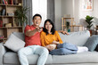 Loving chinese couple resting on sofa, watching TV and laughing
