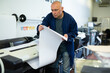 Man working in publishing facility, loading large format paper in printer.