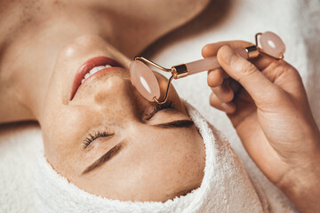 Wall Mural - cosmetologist's hand using jade stone roller for face massage. aesthetic doctor, holding jade stone 