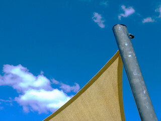 fabric sun shade material spanning over terrace or patio area. blue sky and white clouds. Loosely weaved breathing material. abstract low angle view. canvas patio awning. galvanized pipe post support.