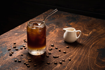 Wall Mural - Cold espresso tonic. A highball glass filled with ice cubes, tonic soda water, coffee beans around, milk jug, wooden background