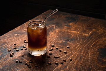 Wall Mural - Cold espresso tonic. A highball glass filled with ice cubes, tonic soda water, coffee beans around, wooden background