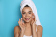 © New Africa - Beautiful young woman with towel applying cream on face against light blue background