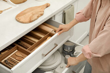 Woman Opening Drawers Of Kitchen Cabinet With Different Dishware And Utensils, Closeup