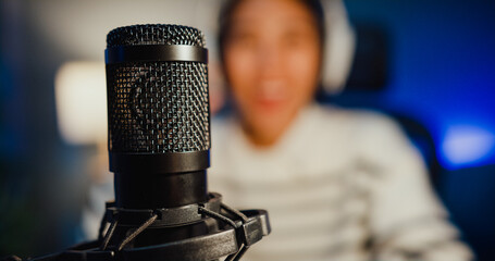 Wall Mural - Happy asia lady blogger music influencer record a podcast on computer with headphones and microphone talk with audience in living room home studio at night. Stay at house, Content creator concept.