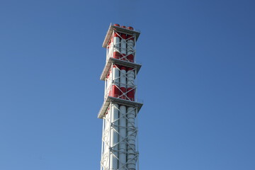 Industrial pipe for ventilation and release of waste into the air, white-red tower of a chemical factory on a sunny day