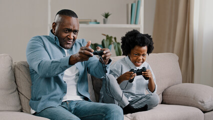 Happy african american family dad and daughter have fun together father playing video game on console with kid girl use controller sit on couch enjoying leisure activity at home winning competition