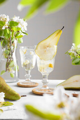 Pear cocktail with pear puree and fresh fruit and flowers on light gray background. Summer cold pear drink lemonade with ice on the table, Sparkling Mocktail dessert beverage with flowering twigs