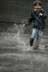 Wall Mural - Child walking in wellies in puddle on rainy weather. Boy under rain in summer