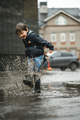 Wall Mural - Child walking in wellies in puddle on rainy weather. Boy under rain in summer