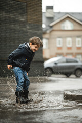 Wall Mural - Child walking in wellies in puddle on rainy weather. Boy under rain in summer