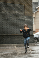 Wall Mural - Child walking in wellies in puddle on rainy weather. Boy under rain in summer